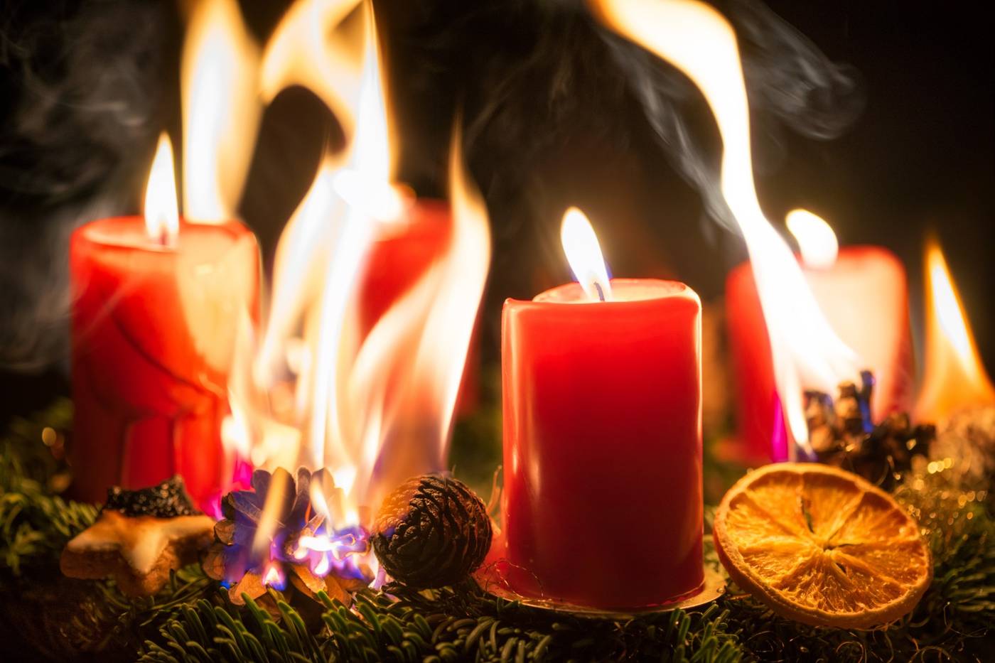Adventskrans med røde stearinlys, hvor grankviste og kogler er gået i brand